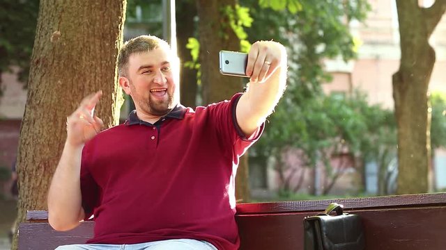 Businessman sits on the bench and makes selfie on smartphone. Man makes photos on mobile phone