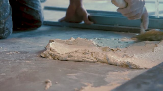 Worker putting cement gum and tiles adhesive on the floor before laying ceramic tile