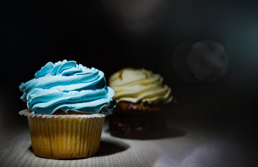 two cupcakes with buttercream on wooden table against dark background with copy space.