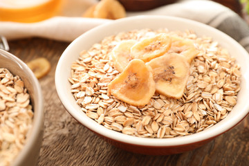 Bowl with oatmeal flakes and banana chips on wooden background