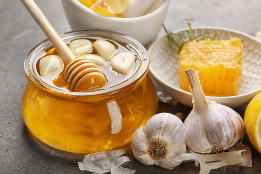 Glass jar with honey and garlic on table, closeup