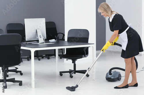 Mature Charwoman Hoovering Floor In Office With Vacuum Cleaner