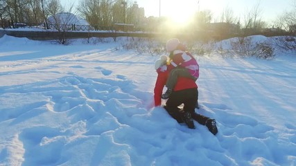 Little girl piggybacking mother in slow motion. Mother playing with daughter in sunny winter park. Happy winter fun on snow