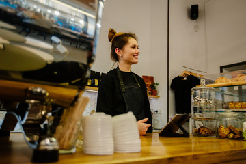 Portrait of cheerful smiling female barista waiting for client while having job in cafe. Labor concept