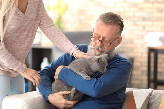 Caregiver giving cute cat to senior man at home