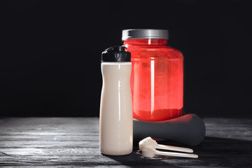 Composition with protein powder, shake  and dumbbell on table against dark background