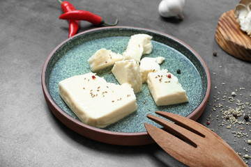Plate with cheese and cooking utensil on grey background