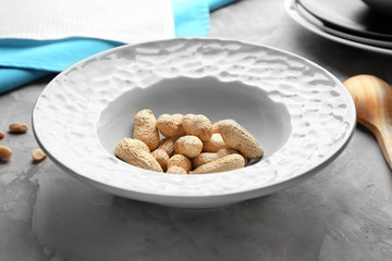 Plate with peanuts on grey background