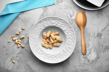 Plate with peanuts on grey background