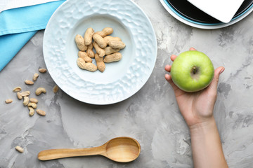 Woman holding apple and plate with peanuts on grey background