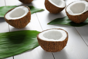 Coconut halves and green leaves on wooden background