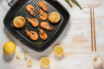 Grilled shrimps on a grill frying pan with lemon, paprika, spices and herbs. Wooden background.