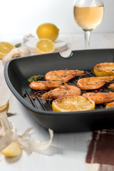 Grilled shrimps on a grill frying pan with wine, lemon, paprika, spices and herbs. Wooden background.