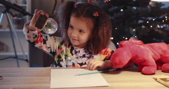 Portrait little girl sit on the table smile hold small toy minature near Christmas tree in home figurine globe holidays joy kids lights child holiday happy tradition winter slow motion