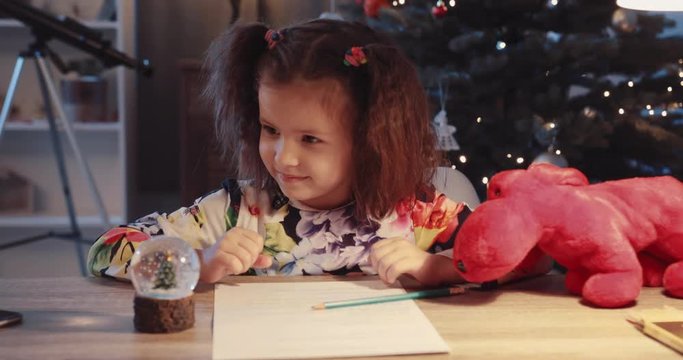 Close up cute little girl sit on the table smile hold small toy minature near Christmas tree in home figurine globe holidays joy kids lights child holiday happy tradition winter slow motion