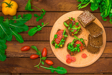 Bruschetta with salmon, red fish, red caviar, arugula and tomatoes on a board. Wooden rustic background. Selective focus. Top view