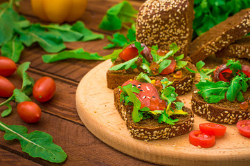 Bruschetta with salmon, red fish, red caviar, arugula and tomatoes on a board. Wooden rustic background. Selective focus. Top view