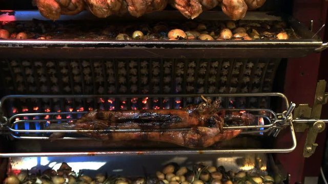 a tilt up shot of a suckling pig, chickens and vegetables being roasted on a rotisserie at a restaurant in paris