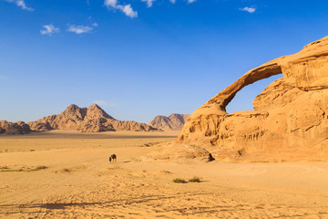 Fototapeta na wymiar Scenic view of the yellow colored arch rock in the Wadi rum desert in Jordan with man and camel walking through
