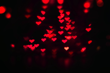 Fototapeta na wymiar Valentine's background with many little luminous red hearts on black, bokeh effect.