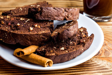 Homemade chocolate biscotti cookies with almonds on dark wooden background on white plate. Close up 