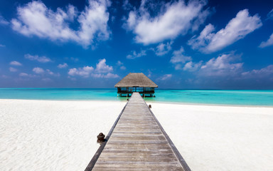 Tropischer Traumstrand mit Holzsteg zu einem Wasser Bungalow über türkisem Meer