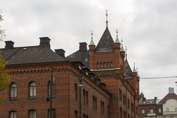 Fototapeta premium Architectural detail of facades of historic red brick houses with turrets in Stockholm, Sweden in a rooftop view against a grey cloudy sky