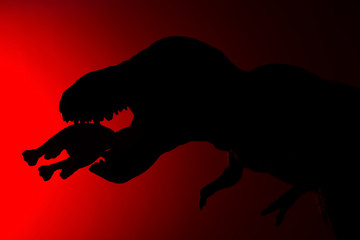 shadow of tyrannosaurus biting a smaller dinosaur with red light in dark