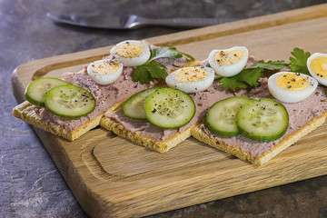 Fresh homemade meat pate on over crispbread on wooden board.