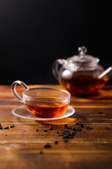 Small transparent cup with black tea on wooden table. Dark background, evening light. Vertical shot, text space.
