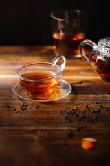 Small transparent cup with black tea on wooden table. Dark background, evening light. Vertical shot, text space.