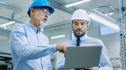 Head of the Department Holds Laptop and Discusses Product Details with Chief Engineer. They Wear Hard Hats and Work at the Modern Factory.