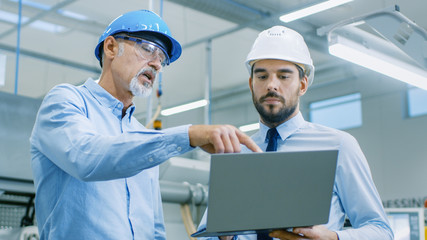 Head of the Department Holds Laptop and Discusses Product Details with Chief Engineer. They Wear Hard Hats and Work at the Modern Factory.