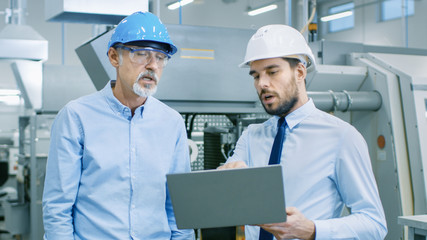 Head of the Department Holds Laptop and Discusses Product Details with Chief Engineer. They Wear Hard Hats and Work at the Modern Factory.