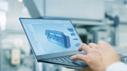 Close-up of the Engineer Holding Laptop with CAD Component Model on Screen. In the Background Modern Factory Equipment. - obrazy, fototapety, plakaty