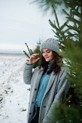 Fototapeta na wymiar Portrait of gentle girl in gray coat and hat against new year tree outdoor.