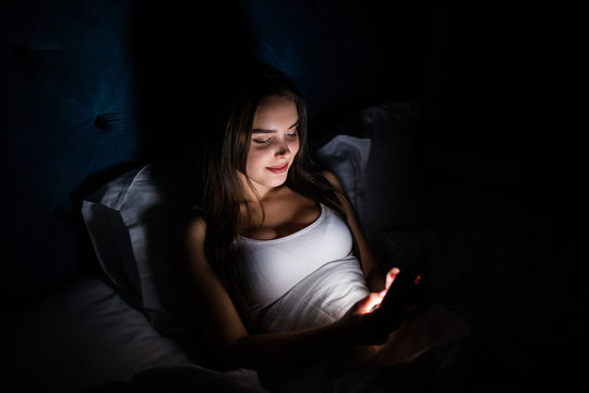 Young woman on bed late at night texting using mobile phone sleepy and tired in internet communication overuse concept and smart phone addiction