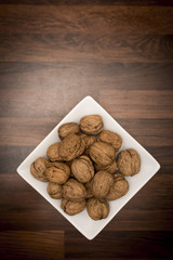A bowl of whole walnuts in their shells in a white square bowl shot from above on a butchers block worktop