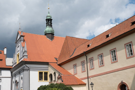 Facade of the Minoritsky klaster (Minorite Monastery) in charming medieval town of Cesky Krumlov, Czech Republic. Belfry of the Minorite monastery, red tiled roof against a cloudy blue sky.