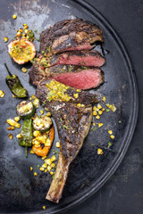 Australian barbecue dry aged wagyu tomahawk steak with vegetable and fruit relish as close-up on an old board © HLPhoto