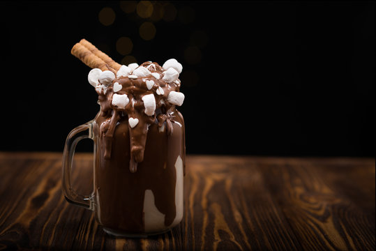 Chocolate milkshake with ice cream and with whipped cream, marshmallow, cookies, waffles, served in glass mason jar. "Freak or crazy" sweet shake. In a black background. Space for text or design.