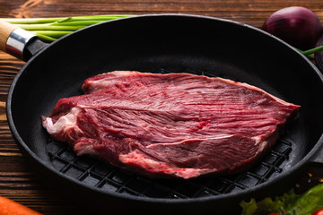 Beef steak in a frying pan with spices, cherry tomatoes, lettuce and carrot.