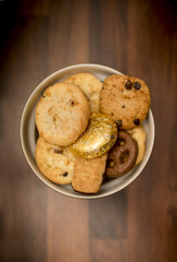 Delicious, yummy and luxurious bowl of luxury biscuits including chocolate chip shortbread cookies, chocolate digestives and orange creme biscuits in a bowl on a butchers block worktop