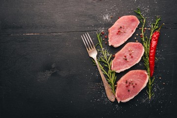 Raw meat. Beef steak with rosemary and spices on a black wooden background. Top view. Free space for text.