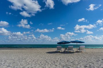 USA, Florida, Empty miami beach with two blue sunshades and three deck chairs in front of the blue ocean