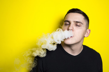 young attractive man with a modern haircut enjoys smoking an electronic cigarette and blows clouds...