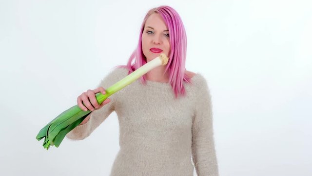 A young woman is biting into a leek and then she is chewing it.