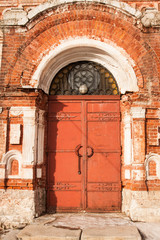 Fototapeta na wymiar Aged Old Red Metal Door On Old Brick Red Facade. Ancient Style.