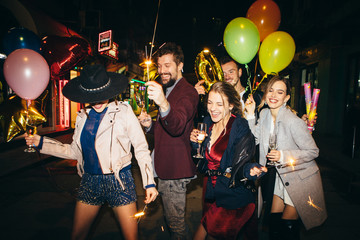 Group of happy friends going on the party, having fun at the street and drinking champagne. New year party. Birthday party 