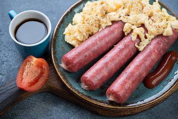 Close-up of a turquoise plate with marbled beef sausages and scrambled eggs, selective focus, studio shot